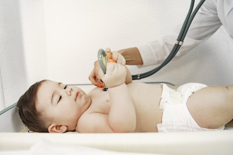 Pediatrician in a white coat examines baby with a stethoscope